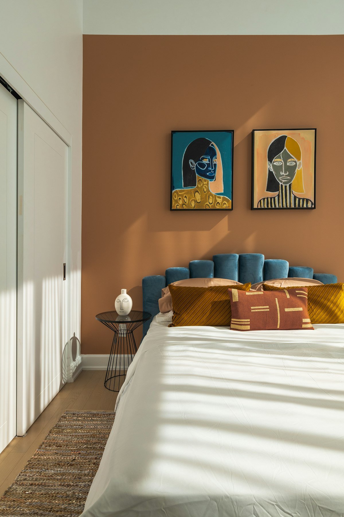 Chambre au mur caramel, tête de lit en velours bleu et coussins ocre